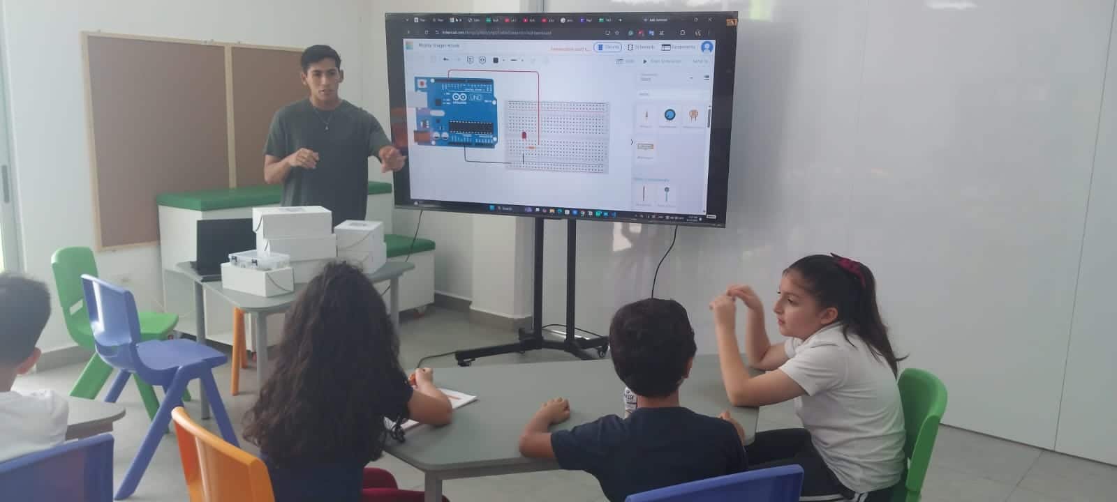 Un instructor explica un circuito con Arduino en una pantalla a tres estudiantes sentados en una mesa durante una clase de robótica